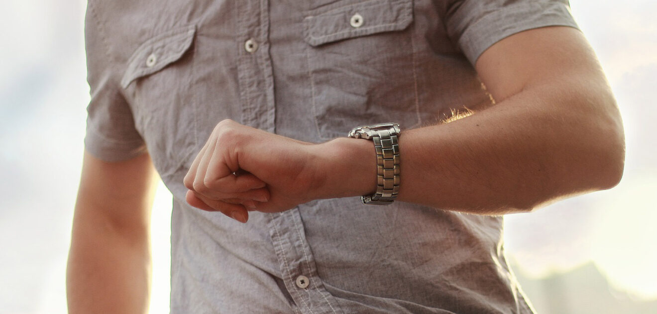Das Foto zeigt einen gut gekleideten Herren, der gestresst auf seine Armbanduhr blickt.