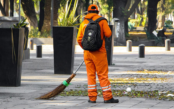 Das Foto zeigt einen Straßenkehrer in einem orangenen Anzug.